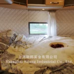 Airstream Allie midsize caravan interior bed with quilted padded walls, floral bedding, small window and soft fur throw
