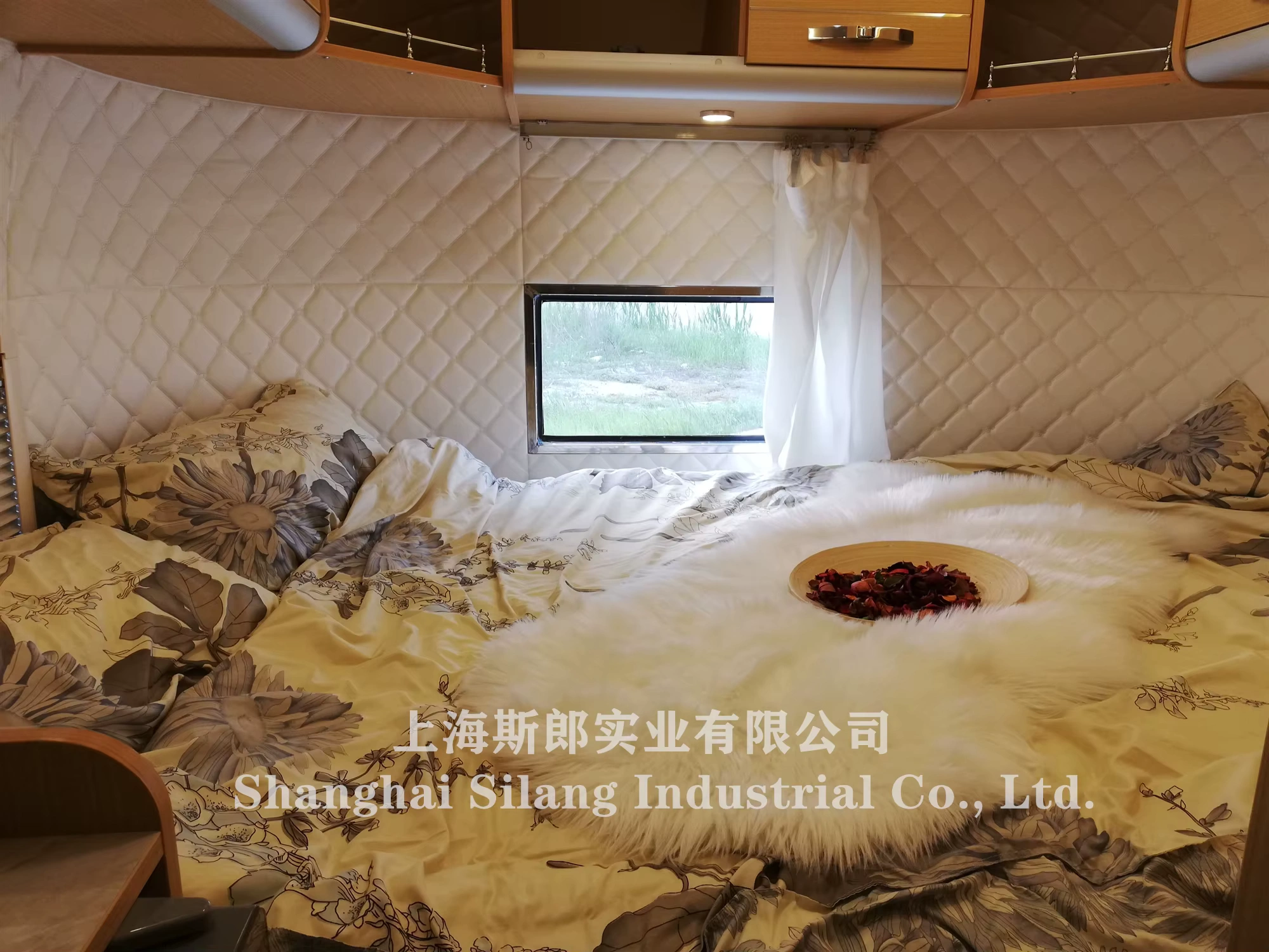 Airstream Allie midsize caravan interior bed with quilted padded walls, floral bedding, small window and soft fur throw