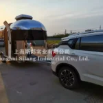 Airstream Allie CODE 2607 stainless steel mid-size caravan hitched to SUV at sunset, highlighting exterior and tow setup