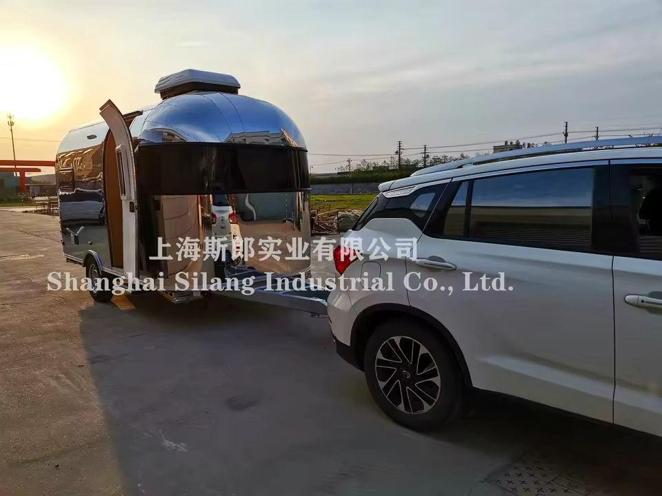 Airstream Allie CODE 2607 stainless steel mid-size caravan hitched to SUV at sunset, highlighting exterior and tow setup