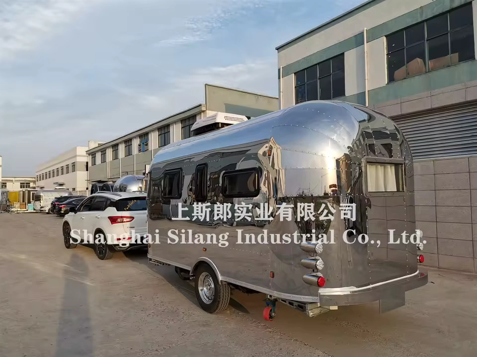 Stainless steel Airstream Allie pop-up caravan parked outside an industrial building, shiny reflective exterior and tow hitch