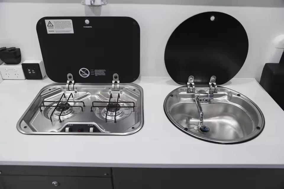 Modern integrated kitchen setup with a two-burner stove and a stainless steel sink for Black Betty Skadoo off-road RVs.