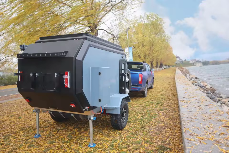Cabin Clam (CODE 2679) off-road camper trailer hitched to a blue truck parked by a lake during an autumn afternoon.