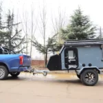 The Cabin Clam (CODE 2679) off-road camper trailer being towed by a blue pickup truck for adventurous travel.