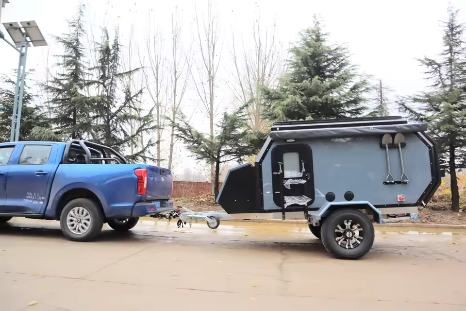 The Cabin Clam (CODE 2679) off-road camper trailer being towed by a blue pickup truck for adventurous travel.