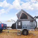 Side view of the Cabin Clam off-road camper trailer hitched to a blue truck, showing the open rooftop tent and features.