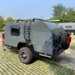Cindy Cinema mini caravan in grey parked on grass pavers, featuring ladder, spare wheel, off-road tyre and awning
