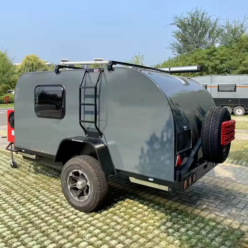 Cindy Cinema mini caravan in grey parked on grass pavers, featuring ladder, spare wheel, off-road tyre and awning