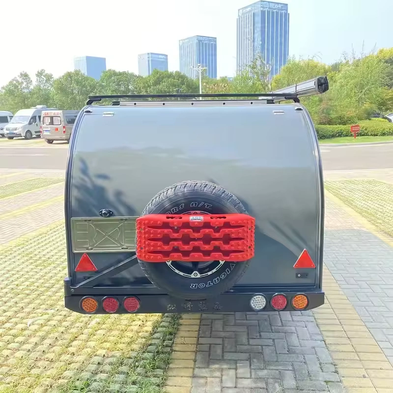 Cindy Cinema mini caravan rear view with spare wheel, red recovery boards, rear lights and rooftop awning in park setting