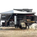 Gutsy Gary off-road camper trailer parked on sand with awning, slide-out stainless steel outdoor kitchen and camping chairs
