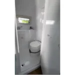 Compact white caravan bathroom interior with cassette toilet, small sink, porthole window and waterproof fiberglass walls
