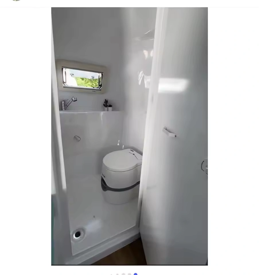 Compact white caravan bathroom interior with cassette toilet, small sink, porthole window and waterproof fiberglass walls