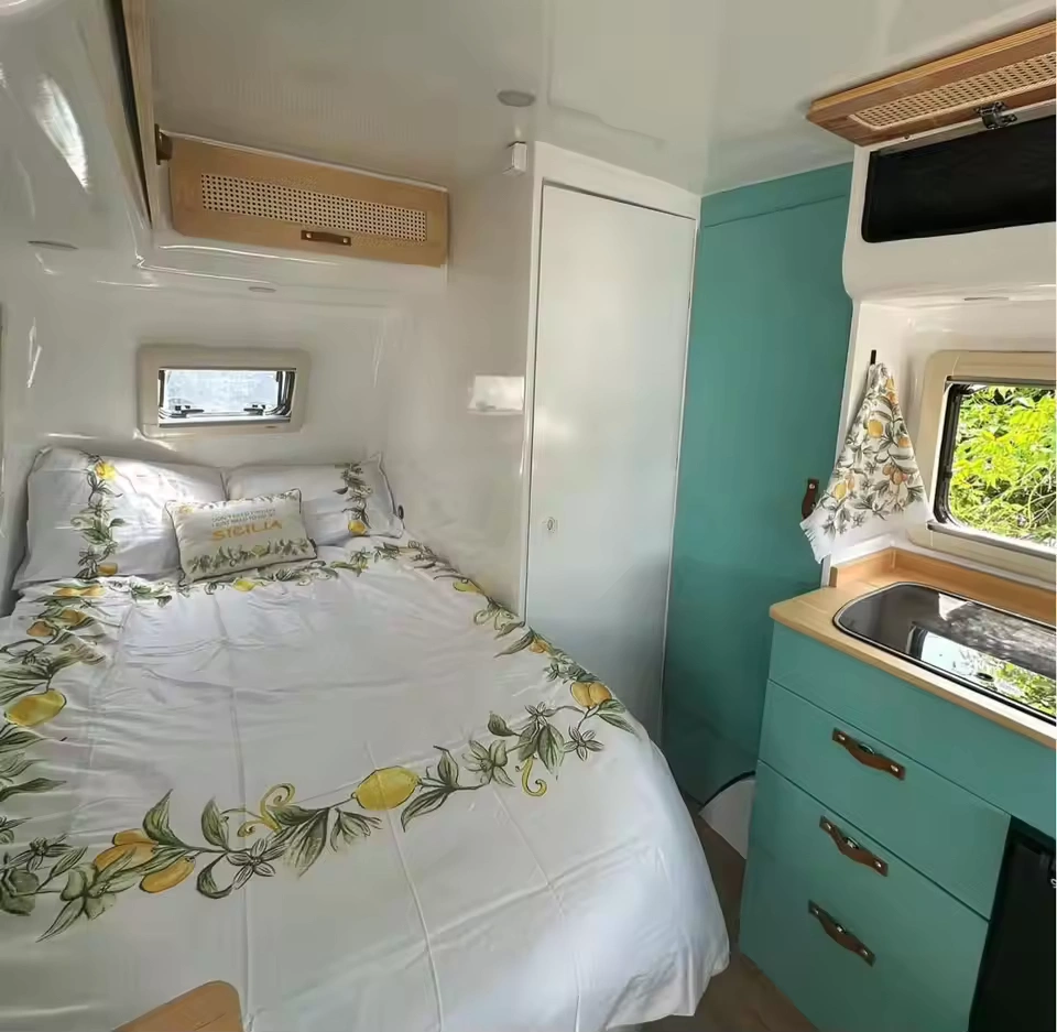 Molly Moulds midsize caravan interior featuring queen bed with lemon design bedding and teal kitchenette drawers
