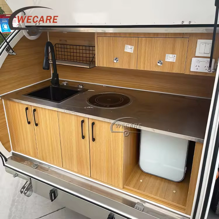 WECARE off-road teardrop caravan slide-out kitchen with sink, induction cooktop, wooden cabinets, and compact fridge.