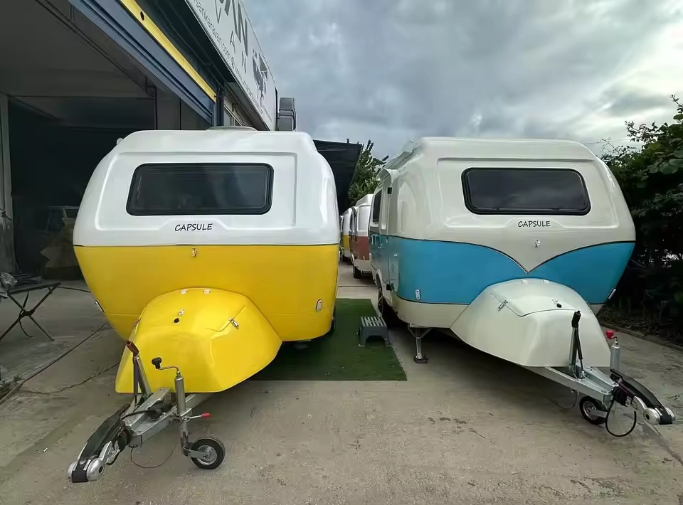 Two compact "Capsule" pop-up caravans in yellow and blue parked side-by-side at a caravan dealer lot, Molly Moulds model