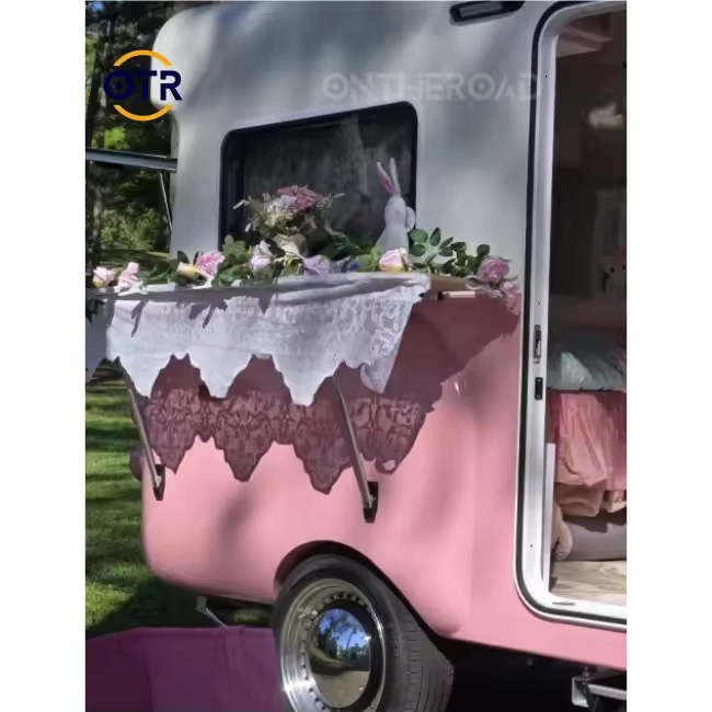 Retro Rex pink teardrop caravan showing lace-draped serving hatch, floral arrangement and open side door for glamping