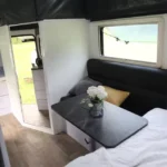 Roming Romeo mini off-road caravan interior showing fold-down dining table, black sofa, bed, window and storage (SEO)