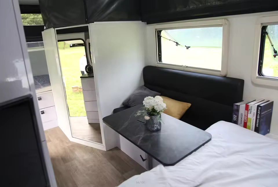 Roming Romeo mini off-road caravan interior showing fold-down dining table, black sofa, bed, window and storage (SEO)
