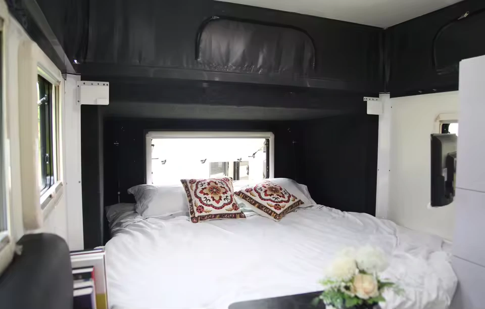 Roming Romeo off-road mini caravan interior featuring queen bed, decorative cushions, white bedding and pop-top canvas roof