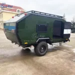Side profile view of the Rugged Roy off-road teardrop trailer featuring a dark green exterior, rugged tires, and roof rack.