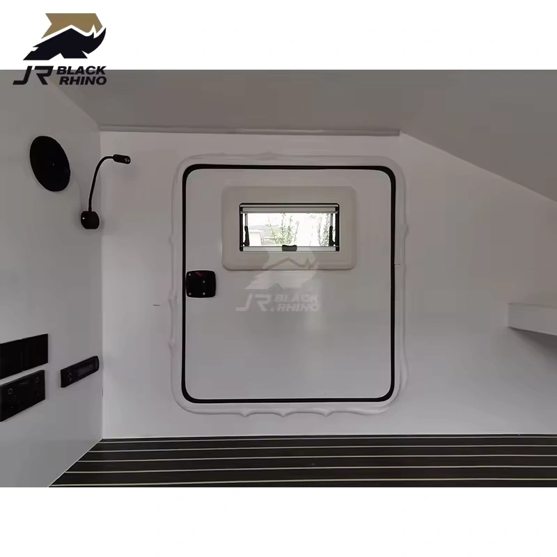 Interior view of the Shark I mini camper trailer featuring a white door, window, wall-mounted lamp, and modern flooring.
