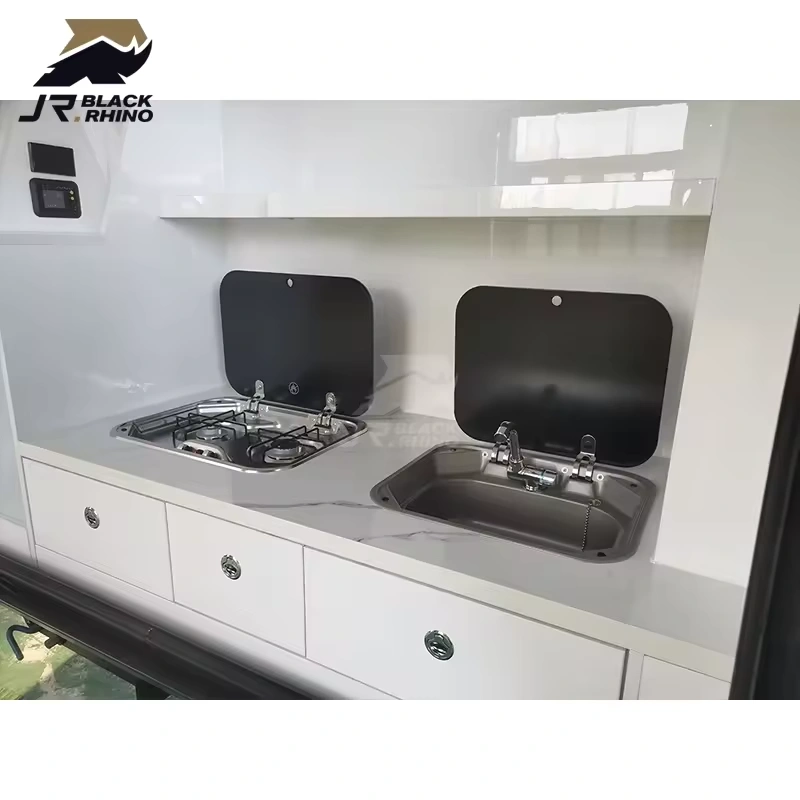 Compact kitchen area inside the Shark I mini caravan featuring a stainless steel stove and sink with modern white drawers.