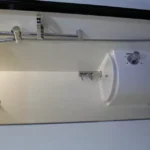 Compact bathroom interior of the Toy Boy caravan featuring a modern shower head, sleek white sink, and chrome faucet.