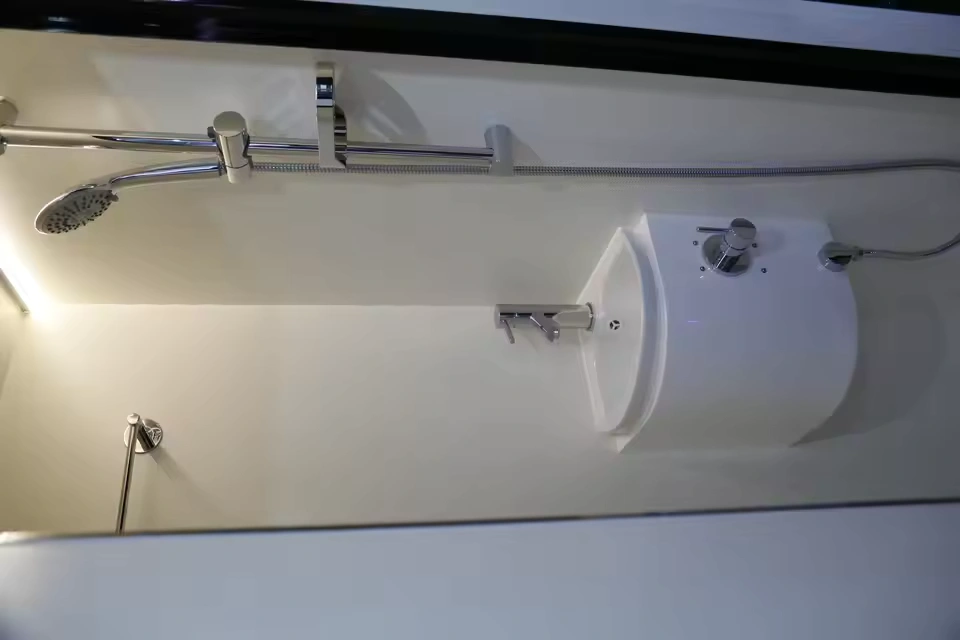 Compact bathroom interior of the Toy Boy caravan featuring a modern shower head, sleek white sink, and chrome faucet.