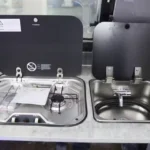 Compact stainless steel two-burner stove and sink combo with protective black lids in the Toy Boy off-road caravan.