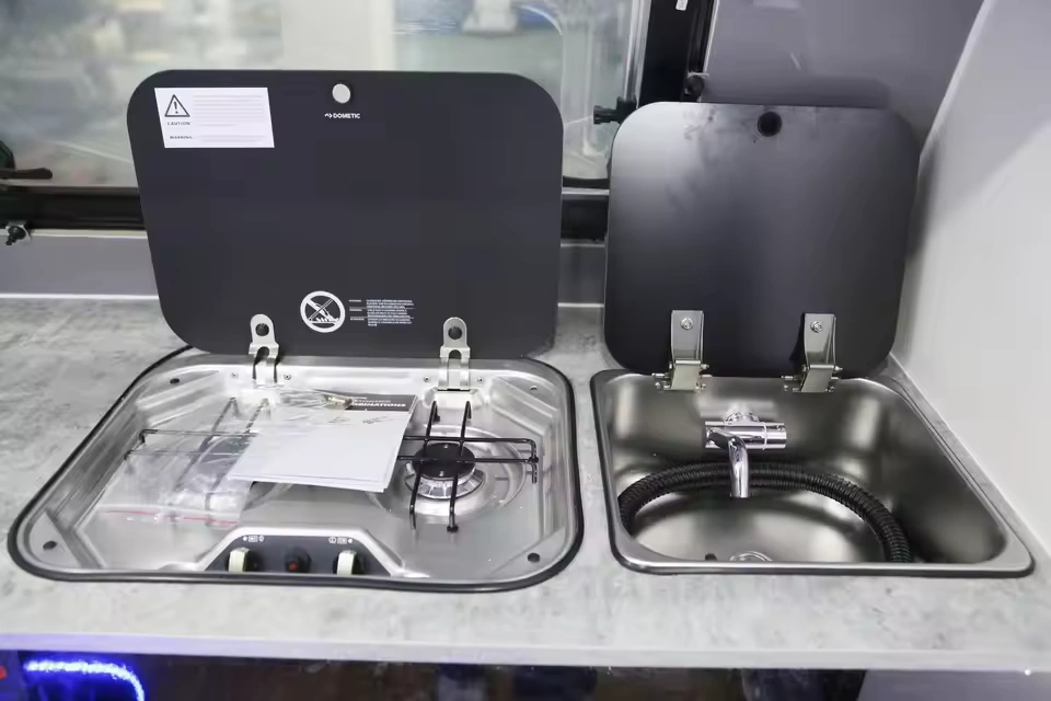 Compact stainless steel two-burner stove and sink combo with protective black lids in the Toy Boy off-road caravan.