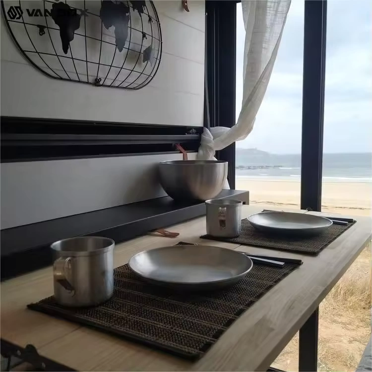 Van conversion interior dining setup with stainless steel plates, cups and bowl by window overlooking sandy beach view