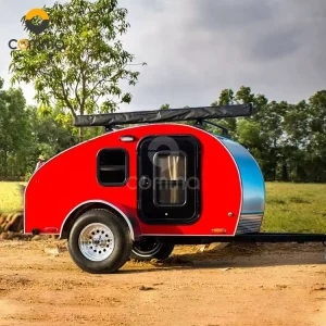Side view of the bright red Cody Compact mini teardrop caravan parked on a dirt field for outdoor camping adventures.