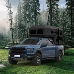 The Larry Light CODE 2685 off-road camper trailer mounted on a blue Ford truck in a scenic forest clearing for travel.
