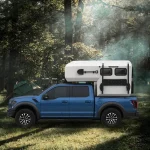 The Larry Light CODE 2685 slide-on camper mounted on a blue pickup truck parked in a scenic forest setting for camping.